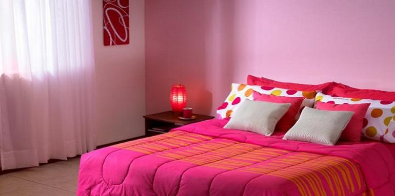 Habitación pared lila con cama doble tendido fucsia