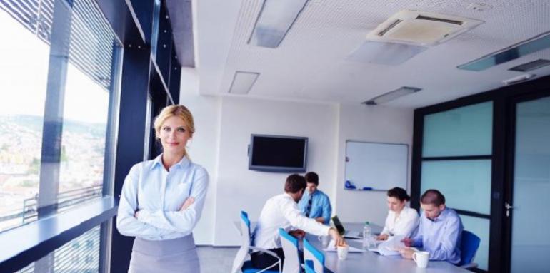 Mujer en oficina junto a mesa con personas reunidas