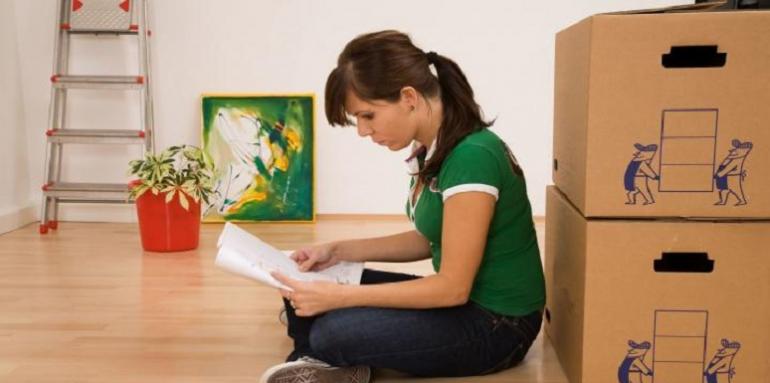 Mujer sentada revisando papeles con cajas de cartón detrás 