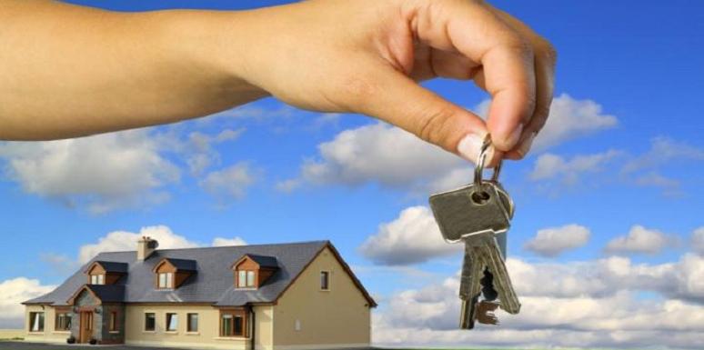 Mano de mujer entregando llaves con casa de fondo